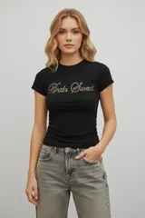 Remera de algodón color negro, de corte ajustado y manga corta, con cuello redondo a la base y estampa frontal con la frase 'Kinda Sweet' realizada en strass.