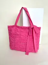 Bolso tipo tote 100% algodón de color fucsia, con diseño drapeado en toda la superficie, doble asa de hombro y detalle de lazo fijo en uno de los laterales.