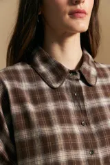 Camisa de estilo leñador con estampado de cuadros en tonos azul, negro y marrón. Presenta cuello clásico, cierre frontal con botones y mangas largas con puños abotonados.