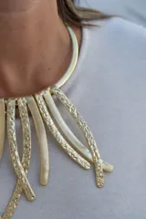 Collar rígido tipo gargantilla con diseño de tiras colgantes de metal dorado, que combinan superficies lisas y texturizadas.