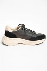 Zapatilla urbana de cuero con diseño de paneles en tonos negro, marrón oscuro y beige. Presenta una suela de plataforma robusta en color beige y cordones jaspeados.