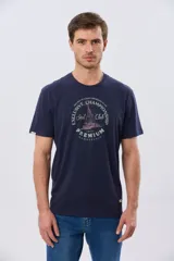 Remera azul marino de manga corta con cuello redondo, confeccionada en mezcla de algodón y poliéster. Presenta un estampado frontal circular de inspiración vintage con diseño de velero y tipografía alusiva a clubes deportivos.
