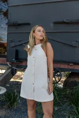 Vestido corto de color beige con cuello halter, diseño sin mangas y cierre frontal con botones dorados.