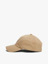 Gorra de béisbol de algodón en color beige, con diseño clásico de cinco paneles, ojales de ventilación y visera curva. Presenta un parche bordado con el logo de Tommy Jeans en la parte frontal y cuenta con una hebilla metálica ajustable en la parte trasera.