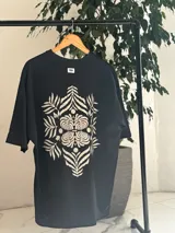 Remera oversize blanca con gran estampado en la espalda de diseño floral simétrico en tono oscuro. Cuenta con mangas cortas y calce holgado.