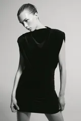Vestido corto de cuello barco y diseño sin mangas con hombreras marcadas. Presenta un acabado satinado con detalle de frunces laterales y en la parte superior, aportando un efecto drapeado.
