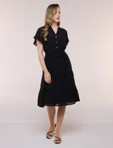 Vestido midi blanco de calce suelto y caída fluida, con escote en V, cuello a la base y apertura abotonada con detalle de puntilla. Cuenta con cintura elastizada con lazo para anudar a tono, mangas cortas con volados y falda con volantes escalonados.