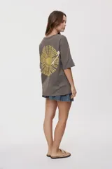 Remera de manga corta y cuello redondo, de corte oversized en color marrón, con texto bordado o estampado a lo largo del escote en el hombro izquierdo.