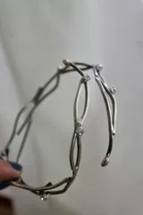 Brazalete rígido plateado con apliques dorados, de alpaca. Se ajusta a presión en el brazo.