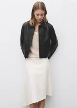 Chaqueta corta de efecto piel en color negro, con cuello de solapa, cierre frontal de botones y dos bolsillos de parche con solapa en la parte delantera. Presenta un diseño recto y forro interior.
