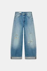 Jeans de tiro medio con corte baggy y bajo acabado en vuelta. Presenta diseño de cinco bolsillos, trabillas para cinturón, cierre frontal con cremallera y botón metálico, con detalles de roturas en el frente.
