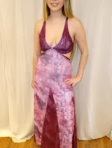 Vestido largo sin mangas con escote en V halter y aberturas laterales (cut-outs) en la cintura. El cuerpo superior presenta un llamativo diseño estampado multicolor, mientras que la falda larga es de tejido texturizado brillante en color verde esmeralda con inserciones godet en el ruedo.