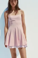 Vestido corto color rosado pálido, con escote cuadrado y tirantes finos ajustables. El bajo tiene un forro con volado de tela a rayas verticales blancas y rosadas.