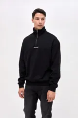 Buzo de felpa con friza, color negro, con cuello alto y cierre frontal parcial. Presenta bordado de la marca en el pecho y un calce relajado.