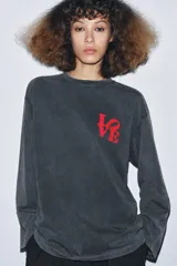 Camiseta de manga larga, corte regular, color negro con efecto lavado o acid wash. Presenta un estampado frontal en rojo con la palabra "LOVE" estilizada.