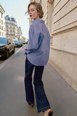 Camisa de corte clásico con cuello solapa y manga larga, confeccionada en tejido oxford con diseño de rayas verticales en azul y bordó. Presenta cierre frontal con botones y bajo con aberturas laterales.