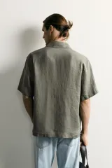 Camisa regular fit confeccionada en tejido de lino, color blanco, con cuello solapa, manga corta y cierre frontal de botonadura.