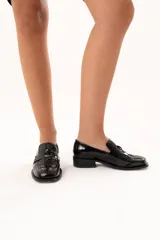 Mocasín de cuero charol negro con diseño enrejillado en la capellada, horma cuadrada y taco bajo.