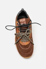 Championes de gamuza color marrón con detalles en cuero liso del mismo tono. Presentan cordones bicolores en naranja y negro, suela de goma plana y un detalle en color rojo en la parte trasera del talón.