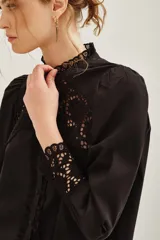 Camisa negra de algodón con detalles de encaje calado en el pecho, hombros y puños. Presenta cuello alto con terminación de encaje, cierre frontal con botones y mangas largas abullonadas.