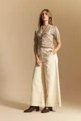 Pantalón largo color crema, tiro alto, de corte recto y ancho. Presenta costuras visibles en contraste y bolsillos delanteros.