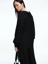 Camisa negra de corte holgado con sutiles destellos brillantes en la textura. Presenta cuello camisero, cierre frontal parcial con botones y mangas largas con puños estructurados.