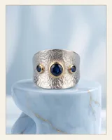Anillo ancho de plata 925 con textura martillada y detalles en oro de 18k, incrustado con tres circonias azules.