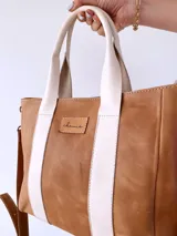 Bolso tipo tote de cuero color camel con dos tiras verticales blancas y correa larga ajustable al hombro.