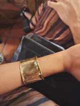 Brazalete rígido de diseño ancho y superficie irregular con acabado brillante, fabricado en bronce y ajustable.