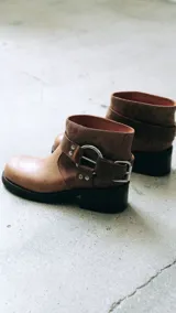Bota corta color marrón de cuero con hebilla plateada y taco bajo.