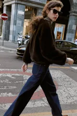 Chaqueta bomber de cuello redondo y manga larga, confeccionada en tejido de pelo sintético color marrón oscuro. Presenta cierre frontal con cremallera, bolsillos laterales y acabados elásticos en el ruedo y puños.