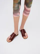 Sandalias planas de cuero color marrón, con diseño minimalista que sujeta el dedo pulgar y deja el empeine al descubierto.