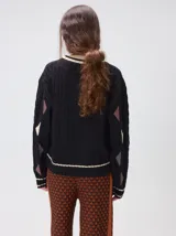 Sweater de punto con diseño de ochos en color verde, cuello redondo con detalle de franja en contraste, y apliques de rombos en las mangas. Presenta un bordado con la letra M en el pecho.