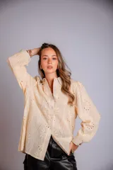 Camisa blanca de broderie, con cuello clásico, cierre frontal con botones, mangas largas abullonadas y puños con botón.