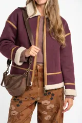 Campera tipo gamulán de color bordó, con interior y cuello de corderito sintético en tono crema. Presenta detalles de ribetes en cuero sintético color suela, cierre frontal metálico y bolsillos laterales.