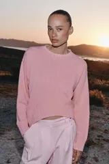 Sweater de punto color rosado con cuello redondo y manga larga, de bajo asimétrico con acabados en rib.