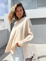 Sweater oversize de tejido de punto color crudo, con cuello redondo, manga larga con puños acanalados y detalle de costura vertical central. Presenta un diseño holgado con aberturas laterales en el ruedo.