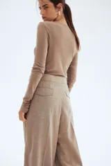 Pantalón sastrero de corte amplio y tiro alto, color beige/tostado con textura sarga. Presenta pinzas frontales y pliegues marcados en las piernas. Tiene cierre con botón y corchete ocultos, y detalles de ajuste con botones forrados en la cintura trasera.