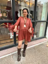 Vestido corto color terracota de tela liviana y translúcida, con escote en V y cordón para atar en el cuello. Presenta mangas largas amplias con puños decorados con volados y diseño fluido de corte evasé.