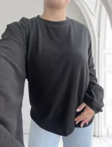 Blusa negra de tejido acanalado con cuello redondo y mangas largas.