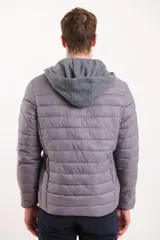 Campera capitoneada color azul marino, con capucha de algodón gris desmontable y cierre frontal. Tiene dos bolsillos exteriores con cierre.