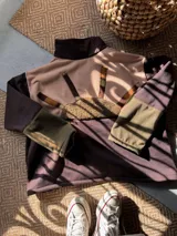 Buzo oversize de friza de algodón y poliéster, con diseño colorblock en tonos verde militar, marrón y rosado. Cuenta con cuello alto, solapa con botones frontales y mangas largas.