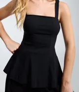 Blusa peplum de bengalina color negro, con escote recto y breteles anchos. Presenta un corte ajustado en el torso con un dobladillo con volados que aporta volumen y estructura a la silueta.