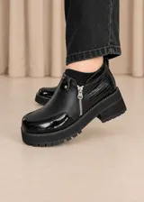 Zapatos de cuero negro con plataforma y suela dentada, combinación de texturas con detalles en charol y cierre lateral.