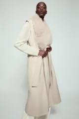 Chaleco largo de mezcla de lana color beige, de corte recto con manga sisa. Cuenta con cuello solapa con aplicación de pelo sintético extraíble, bolsillos laterales ocultos y un cinturón ajustable del mismo tejido para anudar en la cintura.