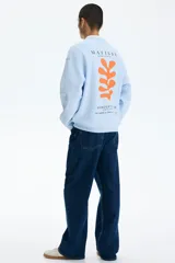 Buzo celeste de corte holgado con hombros caídos y cuello redondo. Presenta un pequeño estampado en el pecho con la inscripción "Matisse" y un detalle gráfico en color naranja.