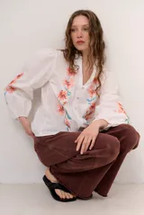 Camisa blanca de manga larga abullonada, con escote en V y bordados florales multicolores en el frente y las mangas.