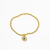 Pulsera elástica de cuentas doradas con dije circular central que presenta un cristal verde rodeado de pequeñas piedras brillantes.