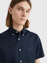 Camisa de manga corta Tommy Hilfiger confeccionada en popelín de algodón, con cuello abotonado y cierre frontal de botones. Presenta un corte regular y el logo de la marca bordado en el pecho.