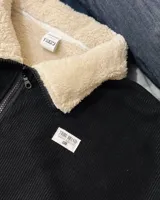 Buzo de pana negra con cierre frontal parcial, cuello alto y forro interior de corderito. Presenta diseño de corte oversized, bolsillos laterales y puños elásticos.